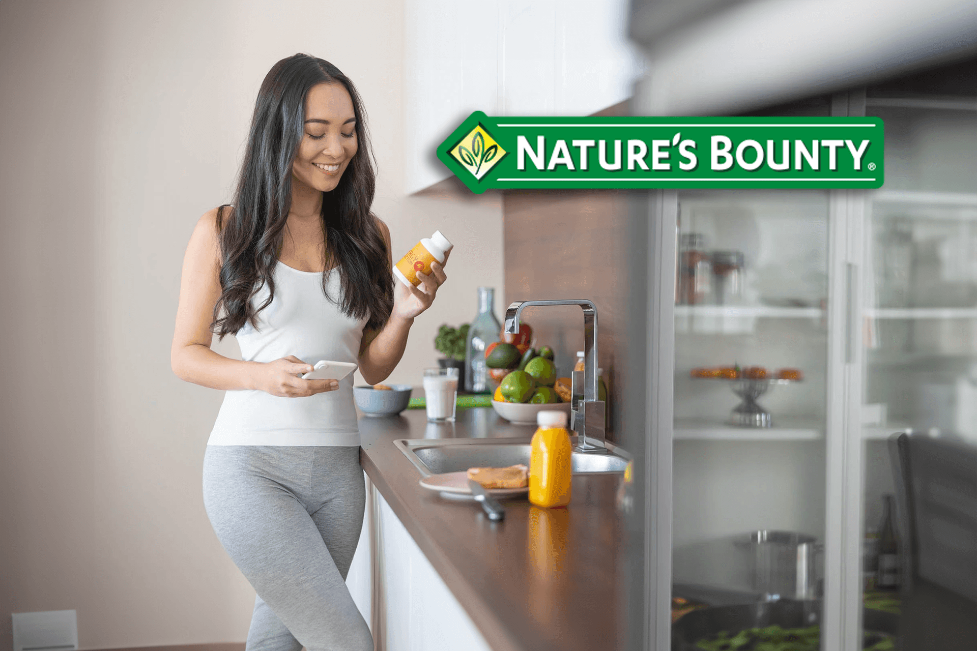 Woman in a kitchen holding a bottle of supplements, with Nature's Bounty logo displayed above.