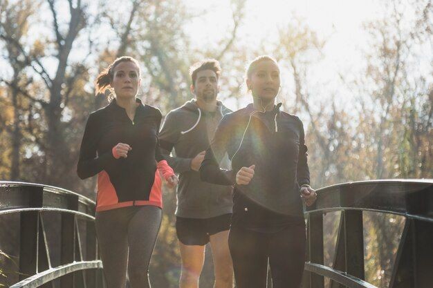 Three people jogging on a bridge in a park during daylight.